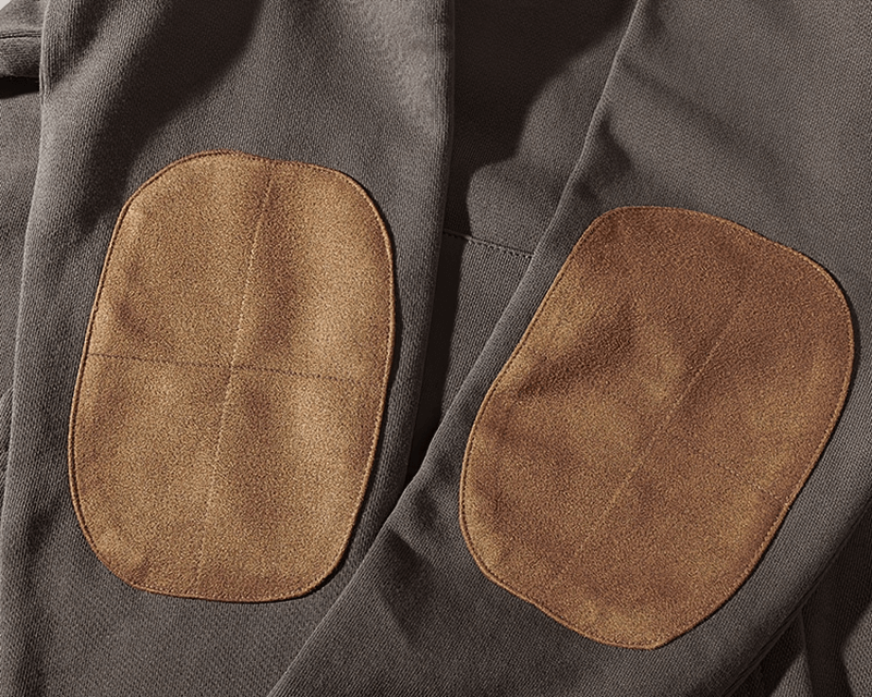 Close-up of brown elbow patches on solid color sweatshirt, highlighting the casual style and durable design of the fabric.